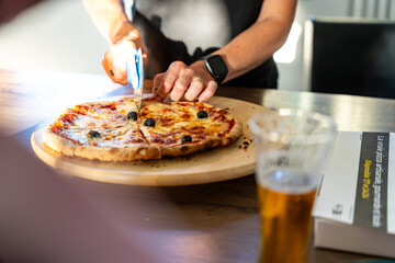 main de femme en train de découper une pizza avec une roulette