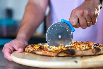 main d'homme en train de découper une pizza avec une roulette