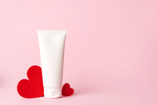 Cosmetic cream white tube with red hearts heart on pink background, copy space