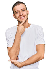 Fototapeta na wymiar Hispanic young man wearing casual white t shirt looking confident at the camera with smile with crossed arms and hand raised on chin. thinking positive.
