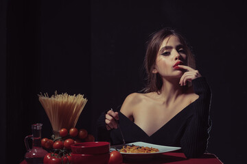 Naklejka premium Eating Spaghetti pasta. Portrait of young Woman Eating Spaghetti pasta. Eating pasta. Woman eat spaghetti with sauce. Good pasta. Girl eats spaghetti. Healthy eating. Sexy kitchen. Finger lick mouth.