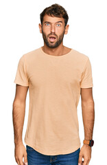 Handsome young man with beard wearing casual tshirt in shock face, looking skeptical and sarcastic, surprised with open mouth