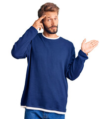 Handsome blond man with beard wearing casual sweater confused and annoyed with open palm showing copy space and pointing finger to forehead. think about it.