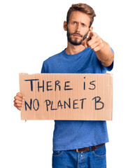 Handsome blond man with beard holding there is no planet b banner pointing with finger to the camera and to you, confident gesture looking serious © Krakenimages.com