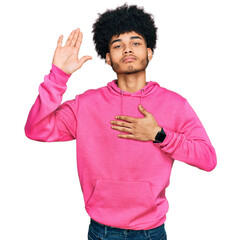 Young african american man with afro hair wearing casual pink sweatshirt swearing with hand on chest and open palm, making a loyalty promise oath