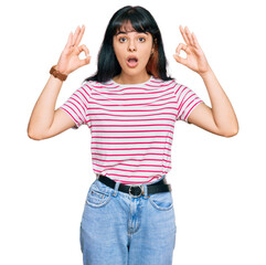 Young hispanic girl wearing casual clothes looking surprised and shocked doing ok approval symbol with fingers. crazy expression