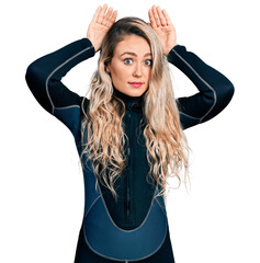 Young blonde woman wearing diver neoprene uniform doing bunny ears gesture with hands palms looking...