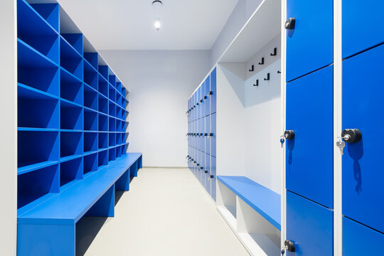 Blue lockers on a wall with key in a lock and cabinet with empty shelves and bench