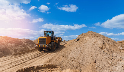 Yellow excavator unloading sand on Open pit mine quarry, sunlight. Concept industrial banner, heavy machinery of construction