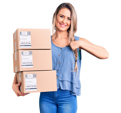 Young beautiful blonde woman holding delivery boxes pointing finger to one self smiling happy and proud