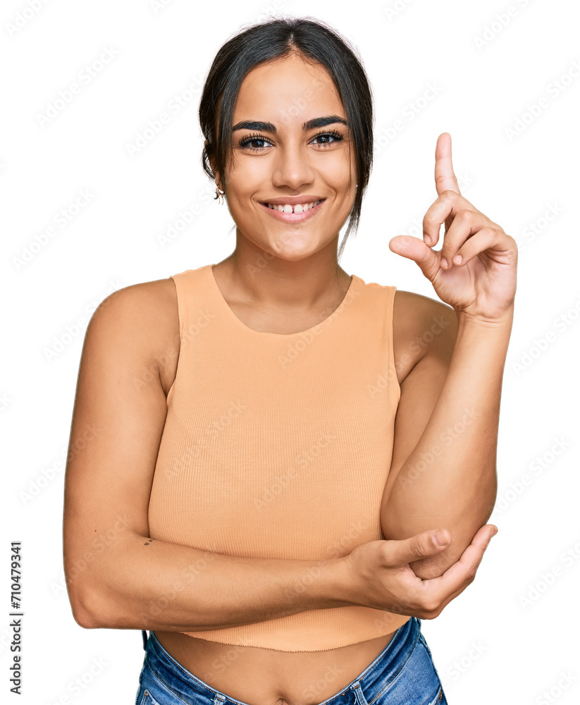 Wall mural Young brunette woman wearing casual clothes with a big smile on face, pointing with hand and finger to the side looking at the camera.