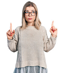 Young blonde woman wearing glasses pointing up looking sad and upset, indicating direction with fingers, unhappy and depressed.