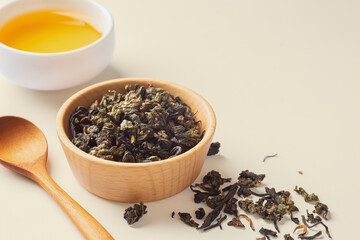 Dried tea leaves in wood bowl with cup of tea on light beige background