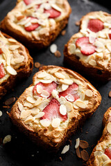 Bostock a French pastry made of sliced brioche with frangipane cream, strawberries and almond flakes, sprinkled with powdered sugar on a black background, close up view