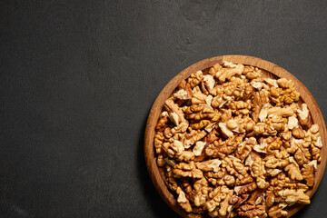 Wooden plate with peeled walnut kernels on a black background with copy space. Top view.