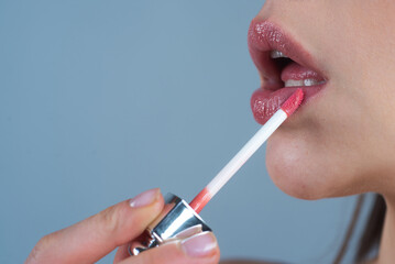 Woman puts lipstick on lips with brush. Close-up of womens hand with lipstick. Applying lipstick on lip. Professional lipstick. plumping lips. Cropped close up photo of girl apply her pomade lip stick