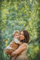 Fototapeta premium Beautiful, happy family on a walk in the park. Son and mother. Mom holds the baby in her arms. Mom looks at her son, and the son looks at his mother. Mom smiles looking at her eldest son. Summer.