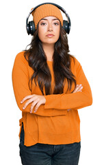 Beautiful brunette young woman listening to music using headphones relaxed with serious expression on face. simple and natural looking at the camera.