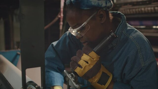 Lowkey waist up shot of young African American female machinery equipment mechanic with flashlight in hand doing repairs at industrial factoryLowkey waist up shot of young African American female mach