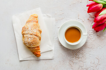 Eine Tasse Kaffee, ein Croissant und rote Tulpen auf einem grauen Tisch. Drausicht.