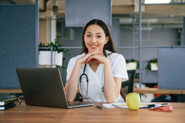 Green apple and laptop on table. Female doctor nutritionist in white coat is indoors