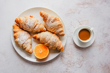 Gebackene Croissant und eine Orange auf einem Teller und eine Tasse Kaffee. Draufsicht.