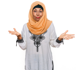 Middle age hispanic woman wearing traditional islamic hijab scarf clueless and confused expression with arms and hands raised. doubt concept.