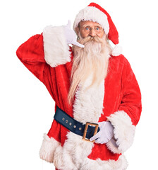 Old senior man with grey hair and long beard wearing traditional santa claus costume smiling doing phone gesture with hand and fingers like talking on the telephone. communicating concepts.