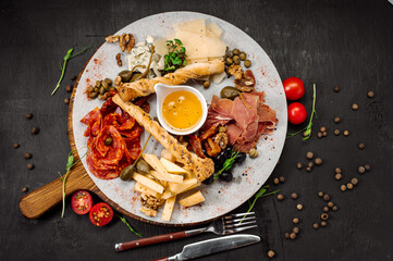 Assorted cuts of dried meat, ham jamon and different types of cheese on a dark background