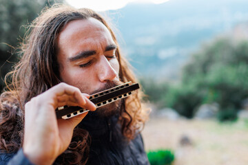 a young man with long hair plays the harmonica. a man enjoys playing the harmonica.