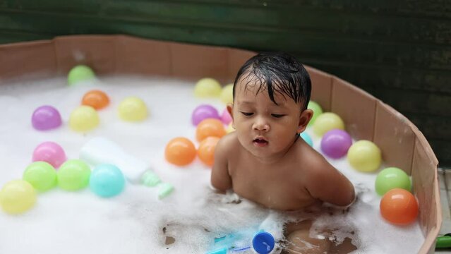 Cute baby  having fun taking bath playing in water with foam with colorful toys.