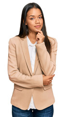 Beautiful hispanic woman wearing business jacket looking confident at the camera with smile with crossed arms and hand raised on chin. thinking positive.