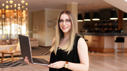 A beautiful business woman works remotely on a laptop in a modern office lobby, the woman smiles and is satisfied with her work.