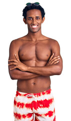 African handsome man wearing swimsuit and sunglasses happy face smiling with crossed arms looking at the camera. positive person.