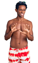 African handsome man wearing swimsuit and sunglasses disgusted expression, displeased and fearful doing disgust face because aversion reaction. with hands raised