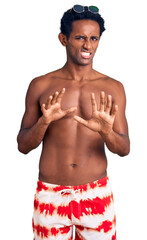 Fototapeta premium African handsome man wearing swimsuit and sunglasses disgusted expression, displeased and fearful doing disgust face because aversion reaction. with hands raised