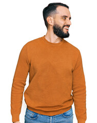 Young man with beard wearing casual winter sweater looking away to side with smile on face, natural...