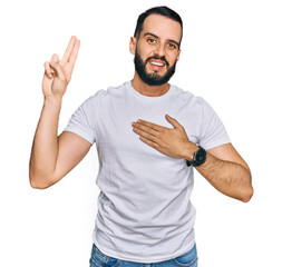 Young man with beard wearing casual white t shirt smiling swearing with hand on chest and fingers...