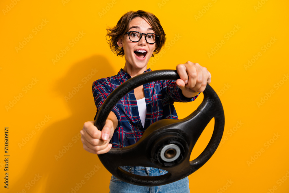 Sticker Photo of funky overjoyed woman dressed plaid shirt in eyewear hold steering wheel driving vehicle isolated on yellow color background