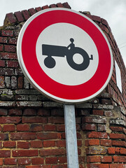 Segnale stradale rotondo con bordo rosso e centro bianco e sagoma di un trattore, che indica divieto di accesso alle macchine agricole gommate e cingolate