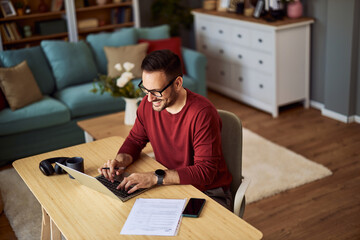 A top view of a smiling male freelancer working and typing on a laptop sitting at a desk at home.