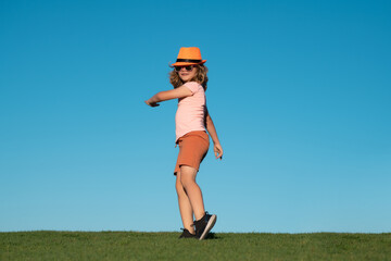 Kid boy running on green grass near blue sky in summer park. Kid boy running outdoor. Sport for children. Runner kids race in park.