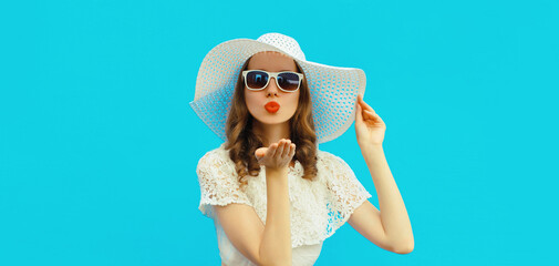 Portrait of beautiful young woman posing blowing her lips sending sweet air kiss wearing white summer straw hat on colorful blue background