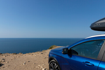 Fototapeta na wymiar A blue car with a roof rack on the edge of a cliff against the blue sky and the sea. Car travel concept.