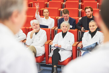 Doctor asking question to speaker holding document at conference