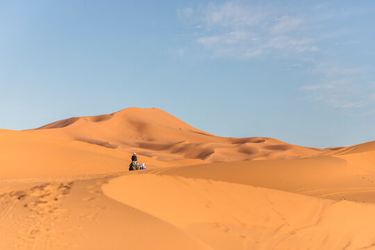 View of a berber bedouin walking across the Sahara Desert with a camel in Merzouga, Morocco.