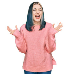 Young modern girl wearing pink wool winter sweater crazy and mad shouting and yelling with aggressive expression and arms raised. frustration concept.