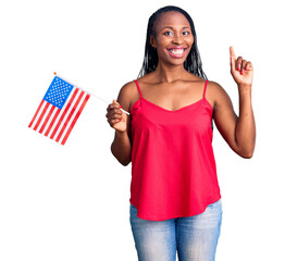 Young african american woman holding united states flag surprised with an idea or question pointing...