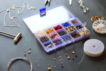 Obraz na płótnie Canvas Box with colorful beads, string, wire, chain, scissors, pliers and hammer on dark background. Various jewelry making supplies. Selective focus.
