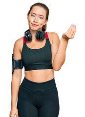 Beautiful blonde woman wearing gym clothes and using headphones doing italian gesture with hand and fingers confident expression